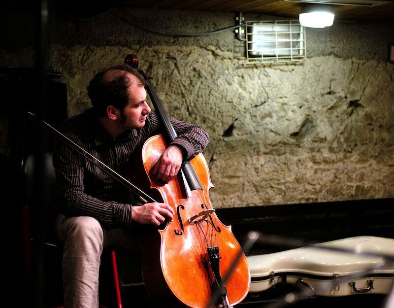Ein Mann spielt Cello in einem Raum mit Steinwänden.