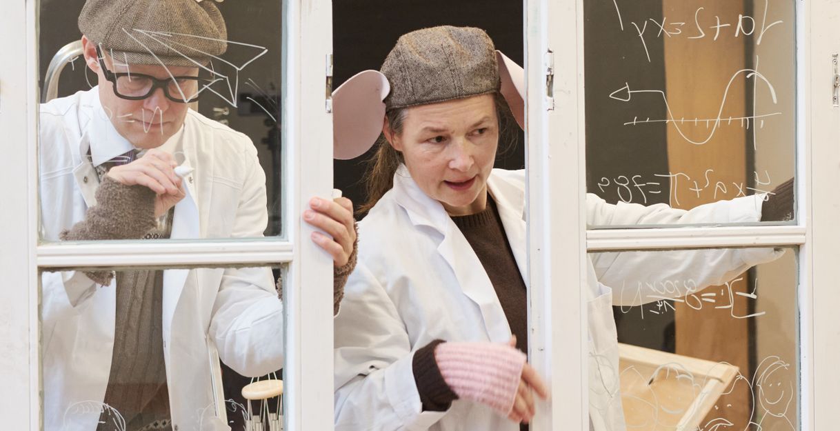 Two scientific looking people, one with mice ears writing formulars at a window. 