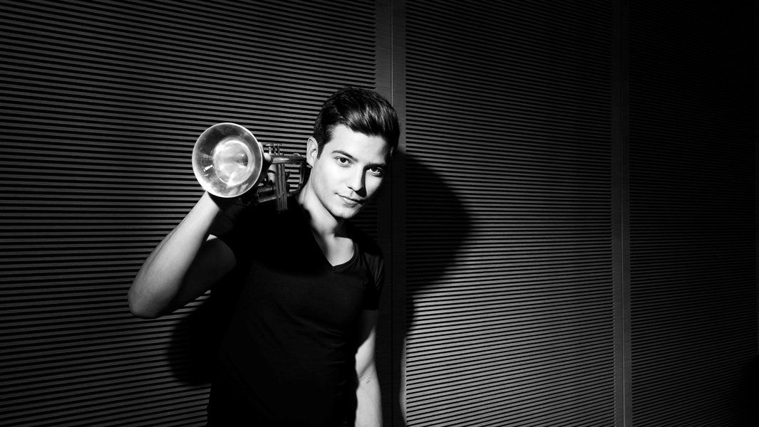 Schwarz-weiß Foto eines Mannes mit Trompete vor einer geriffelten Wand.