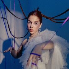 Frau in weißem Kleid mit geflochtenem Haar vor blauem Hintergrund.