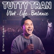 Ein Mann mit Mikrofon auf einer Bühne, lächelnd vor einem Publikum. Text: TUTTY TRAN - Wok-Life-Balance.