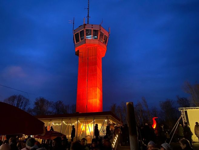 Ein rot beleuchteter Turm bei Nacht mit Menschen im Vordergrund.