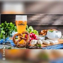 Ein Tisch mit bayerischen Spezialitäten wie Brezel, Weißwurst, Radieschen und einem Glas Bier.