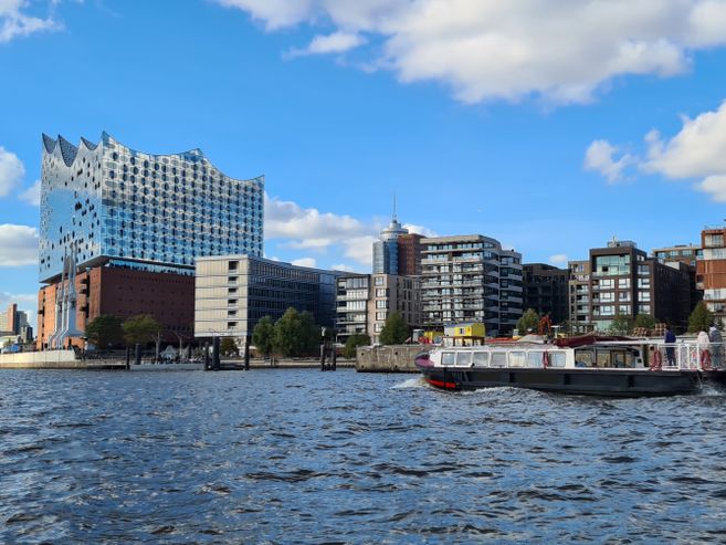 Eine Barkasse fährt auf der Elbe in Richtung der Elbphilharmonie, im Hintergrund stehen viele moderne Gebäude der HafenCity-Skyline