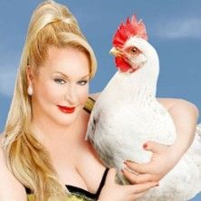 Person mit blondem Haar hält ein weißes Huhn vor blauem Hintergrund.