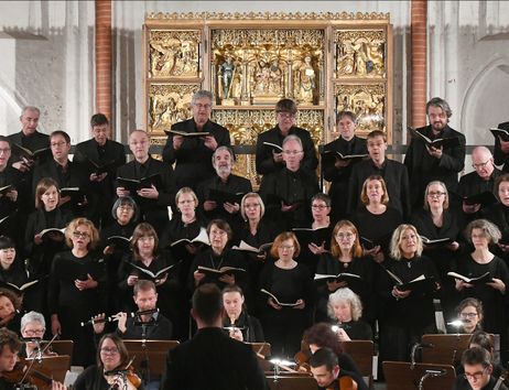 Ein Chor singt vor einem kunstvollen Altar in einer Kirche.