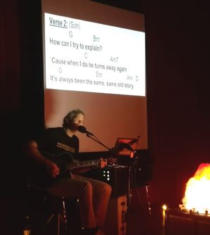 Jan Jahn spielt Gitarre und singt, im Hintergrund wird auf einer Leinwand der Songtext angezeigt