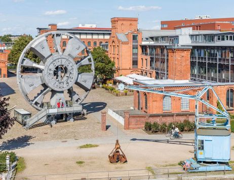 Großes Schaufelrad und historische Backsteingebäude im Freilichtmuseum mit Besuchern.