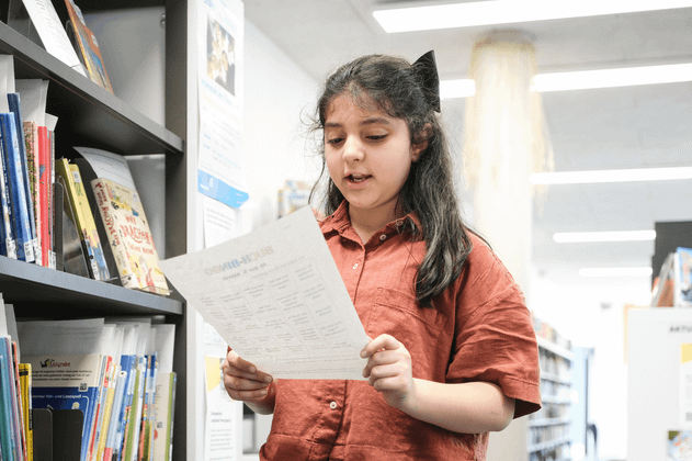 Ein Mädchen liest ein Blatt Papier in einer Bibliothek.