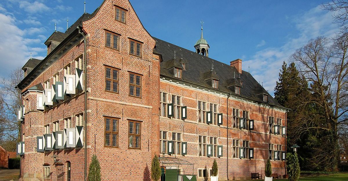 Schloss Reinbek, ein historisches Backsteingebäude mit weißen Fensterläden, umgeben von Bäumen und einem gepflegten Rasen.