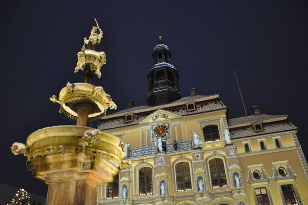 Historisches Gebäude in Lüneburg bei Nacht mit beleuchtetem Brunnen im Vordergrund.