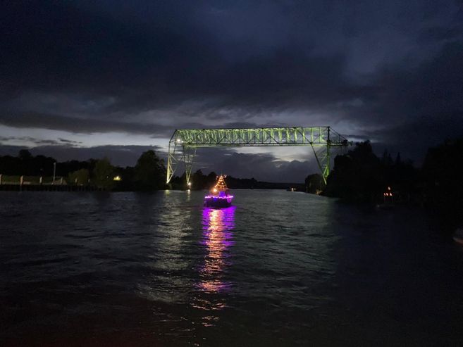 Ein beleuchtetes Boot fährt nachts unter einer Brücke hindurch, die in grünem Licht erstrahlt.
