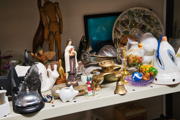 Der Requisitenfundus im SchauSpielHaus. Ein Regel mit diversen Requisiten, darunter ein Schwein aus Porzellan, eine kleine goldene Glocke, ein Männchen aus Holz, eine Marien-Statue und weitere Requisiten.