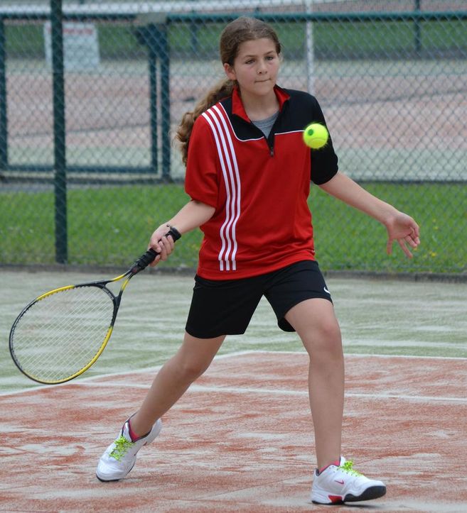 Ein Mädchen in rotem Sportshirt spielt Tennis auf einem Sandplatz.