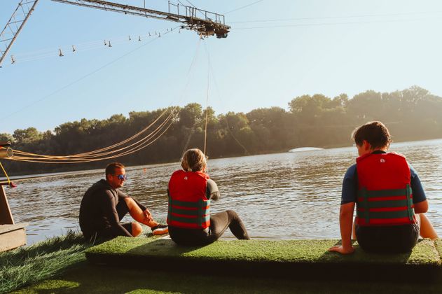 Drei Personen sitzen am Start der Wasserskianlage am Ostesee