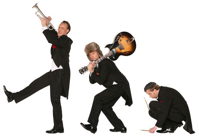 Drei Männer in Frack und Hüten posieren mit Musikinstrumenten vor weißem Hintergrund.