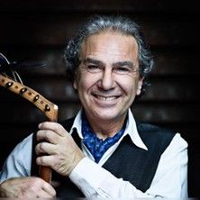 Ein lächelnder Mann mit grauen Haaren hält ein Musikinstrument in der Hand.