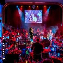 Bühnenauftritt mit Band und Sängerin in buntem Licht.