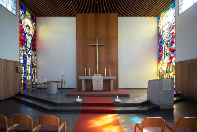 Innenansicht einer Kirche mit Altar, Kreuz und bunten Glasfenstern.
