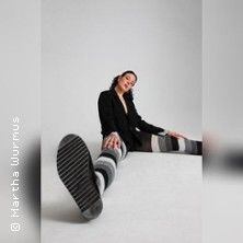 Person sitzt auf dem Boden, trägt gestreifte Strumpfhosen und schwarze Schuhe, fotografiert aus einer niedrigen Perspektive.