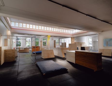 Die Parkourhalle des Fight and Flight Movement Centre mit dunklem Gummiboden und verschiedenen Parkourhindernissen aus Holz sowie Matten. Durch die Oberlichter scheint sanftes Morgenlicht.