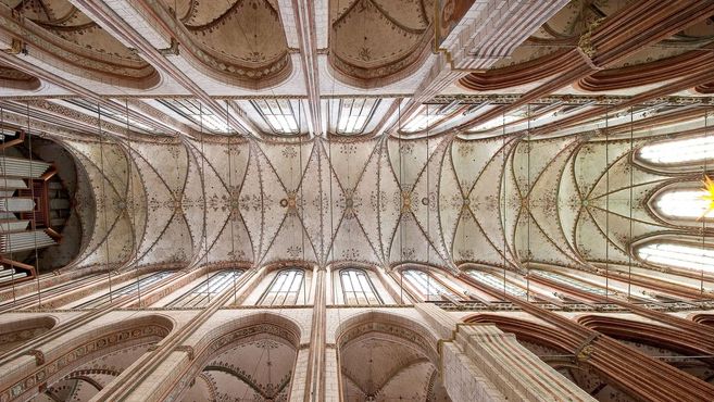 Blick auf die kunstvoll verzierte Decke einer gotischen Kathedrale mit hohen Fenstern und einer Orgel.