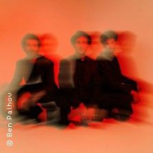 Drei Personen in verschwommenem, rotem Licht sitzen nebeneinander.