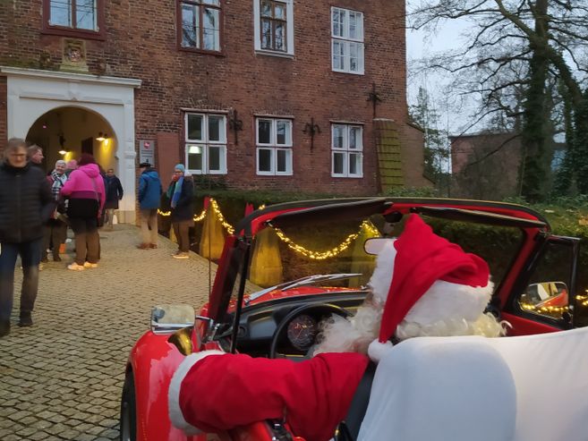 Weihnachtsmann in rotem Auto vor dem Winsener Schloss mit Besuchern.