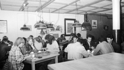 Schwarz-Weiß-Foto von Menschen, die in einem Café an Tischen sitzen und sich unterhalten.