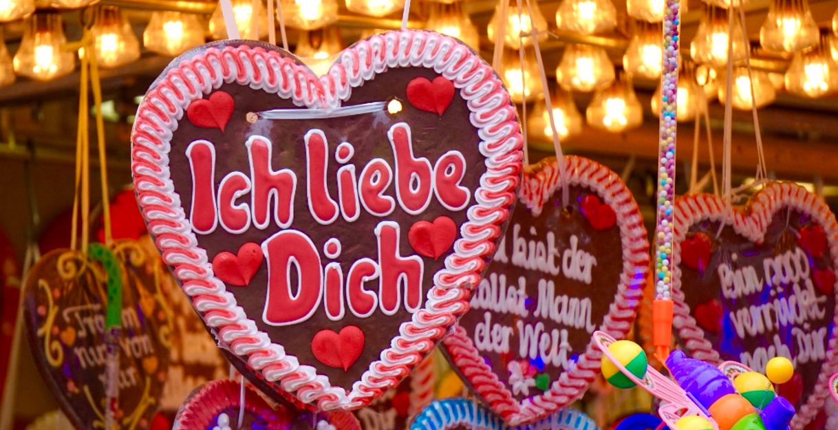Lebkuchenherzen mit Aufschriften wie 'Ich liebe Dich' hängen an einem Stand, umgeben von Lichtern.