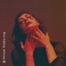 Eine Frau in dramatischer Pose mit rotem Licht und dunklem Hintergrund.