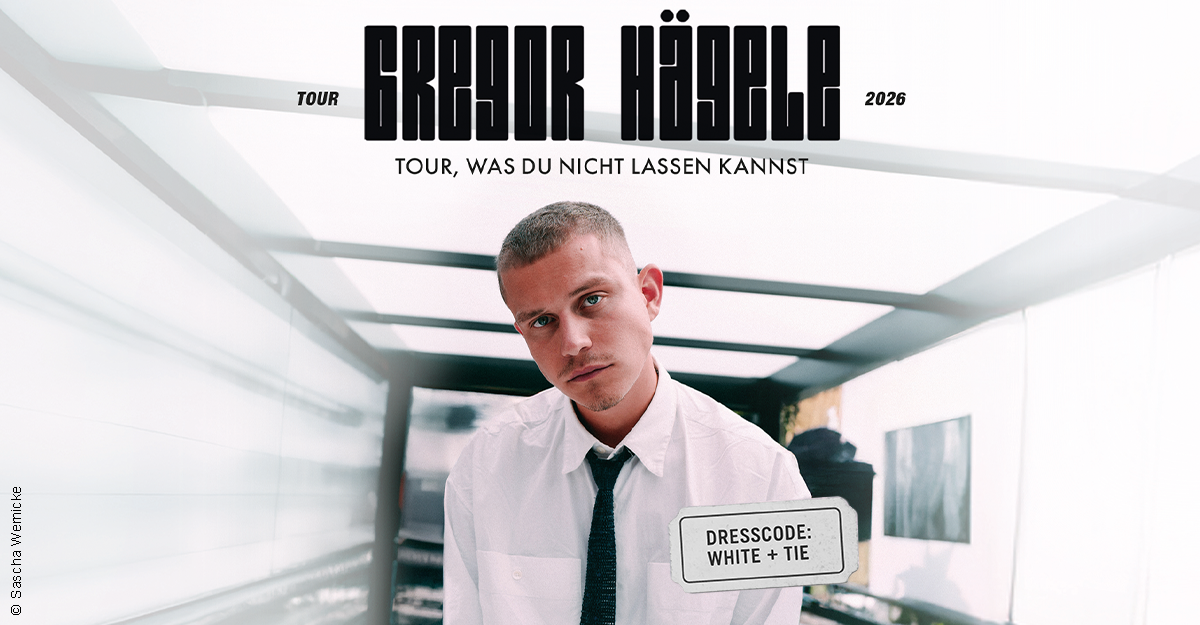 Ein Mann in weißem Hemd und Krawatte steht in einem modernen Raum. Text oben: Gregor Hägele - TOUR, WAS DU NICHT LASSEN KANNST. Dresscode: White + Tie.