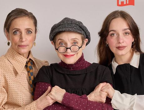 Drei Frauen posieren zusammen, die mittlere trägt eine Brille und Mütze, die anderen zwei haben lange Haare. Im Hintergrund ist ein HF-Logo zu sehen.