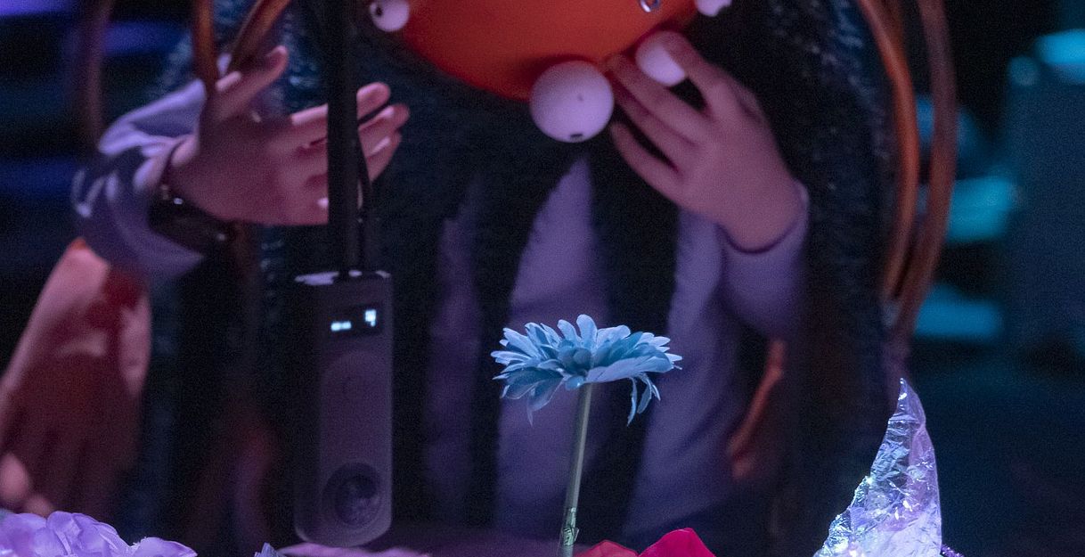Person mit orangefarbenem Helm und Dekorationen bei einer Performance.