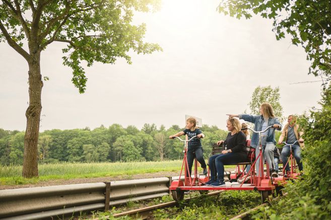 Eine Gruppe von Menschen fährt auf einer roten Draisine entlang einer grünen Landschaft.