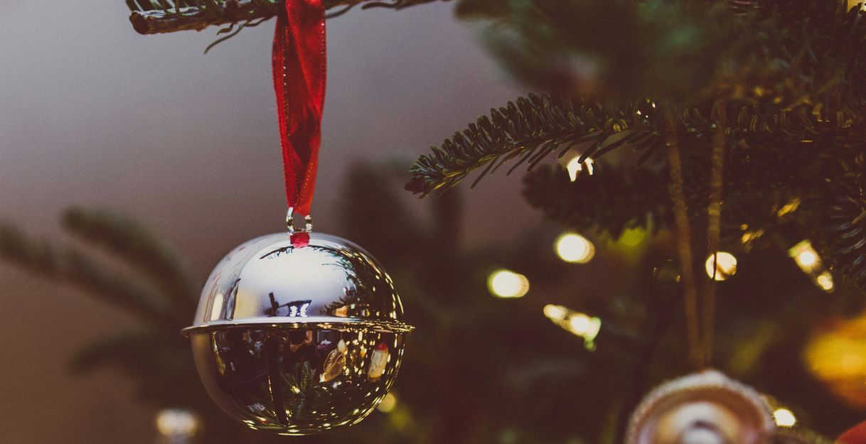 Nahaufnahme einer silbernen Weihnachtskugel mit rotem Band an einem Tannenzweig.