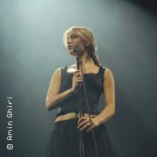 Eine Frau steht auf einer Bühne mit einem Mikrofon in der Hand.