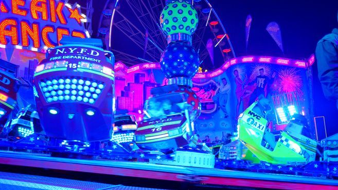 Fahrgeschäft auf einem Jahrmarkt bei Nacht mit bunten Lichtern und bewegten Wagen.