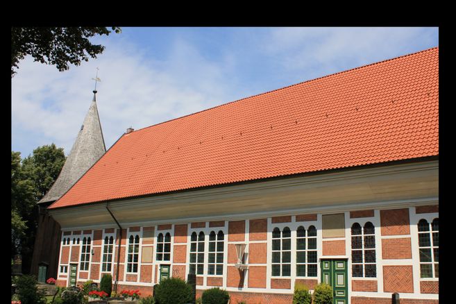 Außenansicht der Dreieinigkeitskirche Allermöhe mit rotem Ziegeldach und Fachwerkfassade.