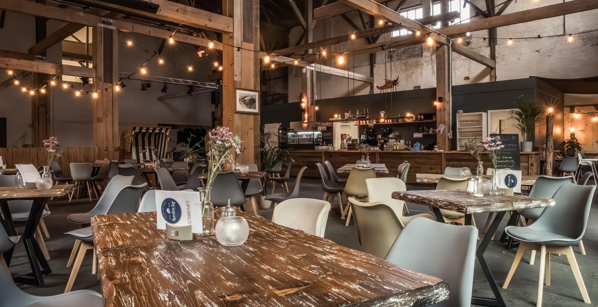 Innenansicht eines gemütlichen Cafés mit Holztischen, modernen Stühlen und Lichterketten.