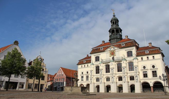 Historisches Rathaus mit Turm und umliegenden Gebäuden auf einem Platz bei klarem Himmel.