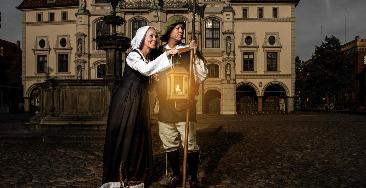 Zwei Personen in historischer Kleidung mit Laterne vor einem alten Gebäude.