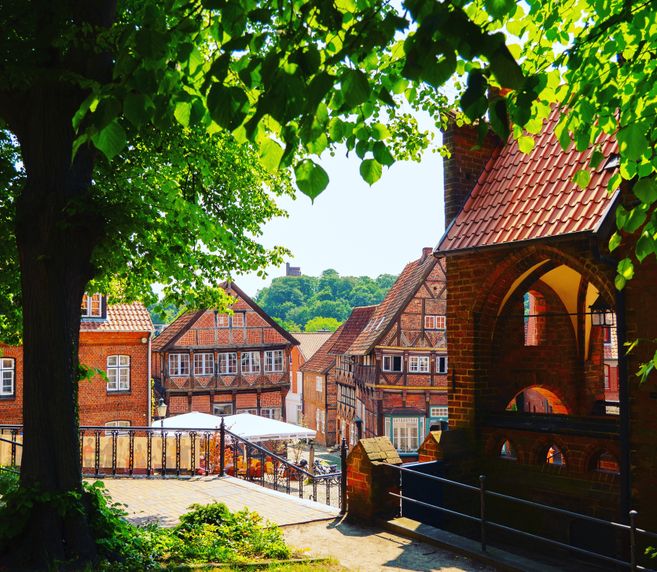 Historische Fachwerkhäuser in einer Altstadt, umgeben von grünen Bäumen und einem Ziegelgebäude im Vordergrund.