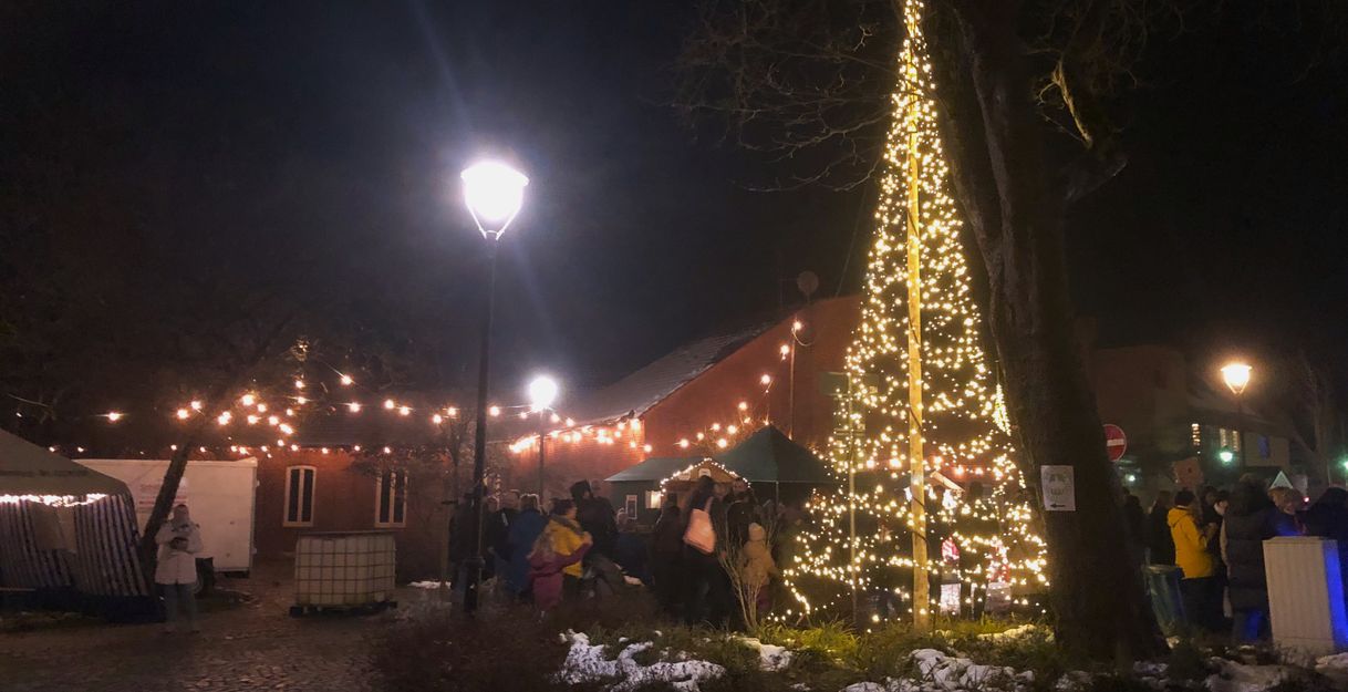 Weihnachtsmarkt bei Nacht mit beleuchtetem Baum und Menschenmenge.