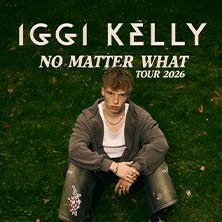 Ein junger Mann sitzt auf einer Wiese, umgeben von grünem Gras. Oben steht der Text: 'Iggi Kelly - No Matter What Tour 2026'.