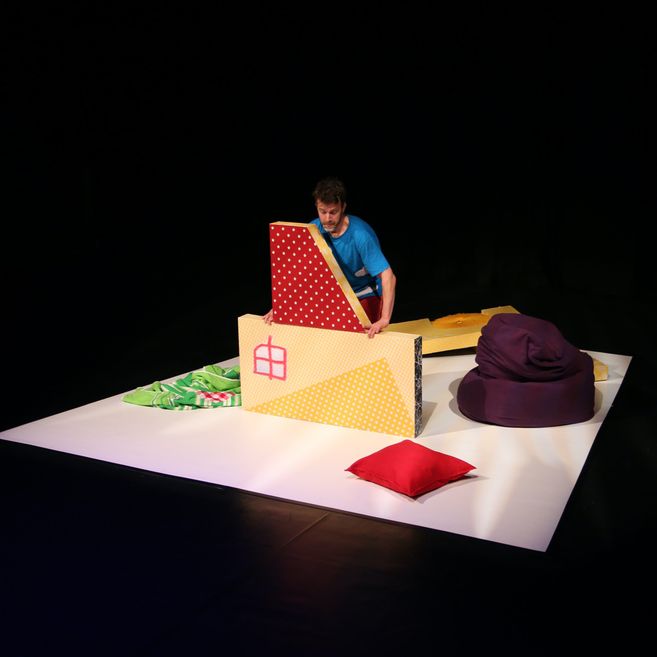 Eine Person arrangiert bunte, gepolsterte Blöcke auf einer Bühne.