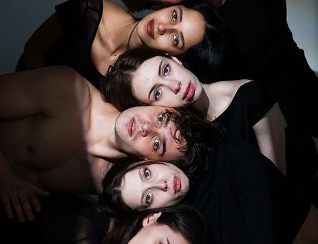 Sechs Tänzerinnen und Tänzer des Hamburger Kammerballetts liegen eng beieinander und blicken in die Kamera.