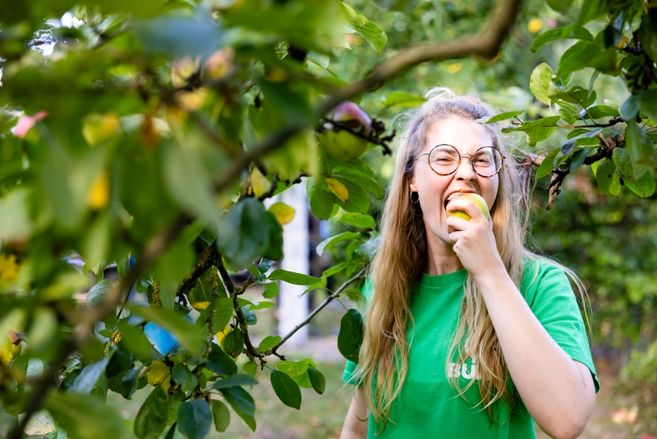 Person unterm Apfelbaum, die in einen Apfel beißt