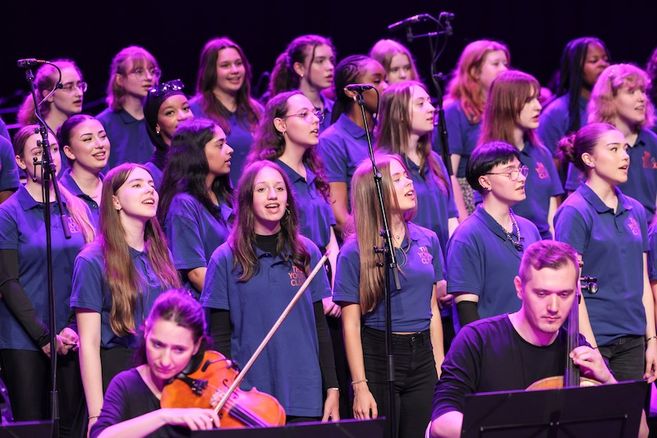 Ein großes Orchester und ein Chor führen gemeinsam auf einer Bühne auf.