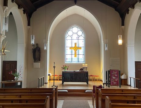Innenansicht einer Kirche mit Altar, Kreuz und Buntglasfenster.